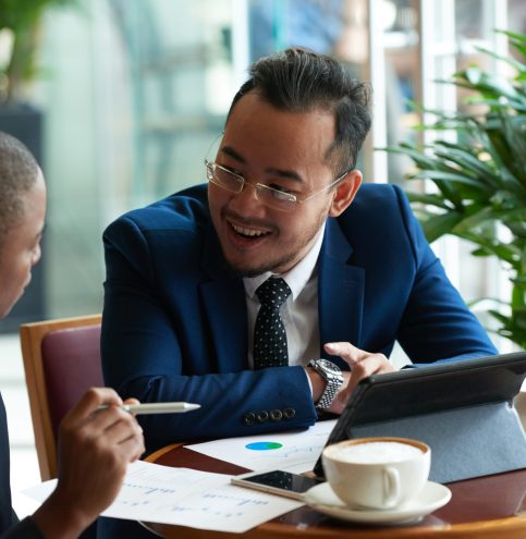 Cheerful Vietnamese businessman having meeting with African-American partner in cafe